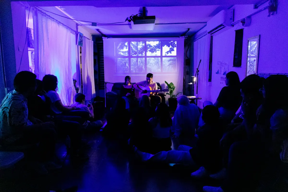 la sala en luz morada, el público sentado en el piso